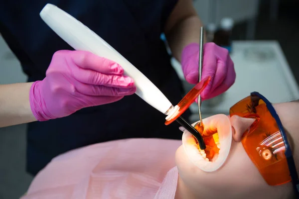 歯医者は病院で患者の歯を治療する 使い捨てゴム口を開ける 歯医者に歯を埋める保護眼鏡をかけた女 — ストック写真