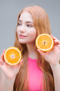 Ellerinde portakalın sulu yarımlarını tutan mutlu, genç bir kadın gri arka planda izole edilmiş. Sağlıklı beslenme konsepti. Diyet.