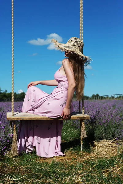 若い美しい女性は 空の背景にラベンダー畑でヴィンテージスイングに座っています — ストック写真