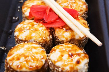 Zencefilli soya soslu fırınlanmış suşi rulosu ve siyah arka planda çubuklar..