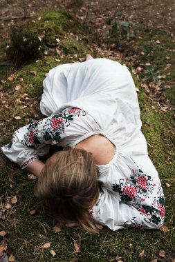 Genç ve güzel bir kadın bir taşın üzerinde yatıyor. Geleneksel Ukrayna işlemeli gömlek. Üst görünüm.