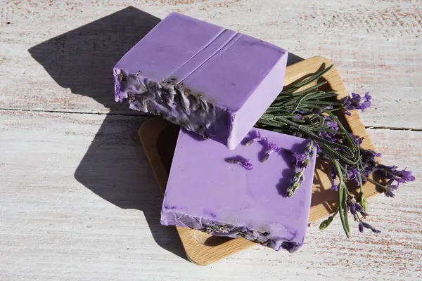 Lavender soap with flowers lying in a soap dish on a vintage wooden board. Top view.