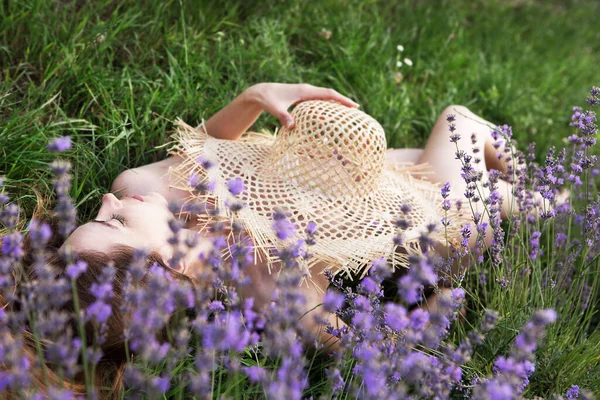 Young beautiful woman sleeps in a lavender field with a straw hat. Healthy sound sleep.