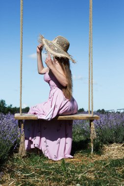 Genç ve güzel bir kadın, gökyüzüne karşı lavanta tarlasında asılı salıncakta sallanırken eğleniyor..
