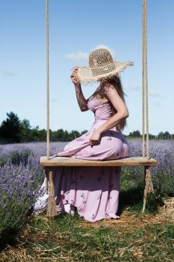 Genç seksi güzel kadın, gökyüzüne karşı lavanta tarlasında asılı salıncakta sallanırken eğleniyor..
