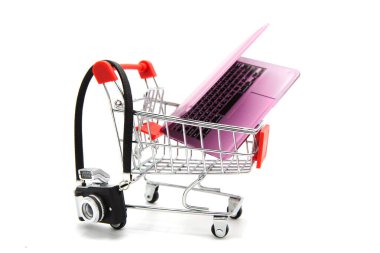 İçinde kamera ve dizüstü bilgisayarla beyaz arka planda izole edilmiş bir süpermarket arabası. İnternetten alışveriş. Elektronik ekipman satın alınıyor.