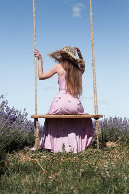 Genç, seksi, güzel bir kadın, gökyüzüne karşı lavanta tarlasında asılı salıncakta güneşin tadını çıkarırken. Arka plan.