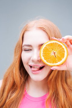 Genç, mutlu, gülümseyen bir kadın, elinde portakalın sulu bir yarısını gri arka planda tutuyor. Sağlıklı beslenme konsepti. Diyet.