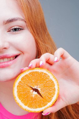 Gri arka planda, portakalın sulu yarısını elinde tutan mutlu, genç bir kadın. Sağlıklı beslenme konsepti. Diyet.