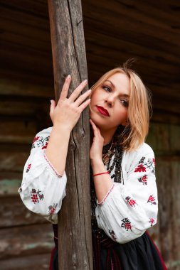 Portrait of a young beautiful woman in a traditional Ukrainian costume against the background of an old wooden wall of a house. Embroidered shirt. Vyshyvanka. Traditional Ukrainian handicrafts. clipart