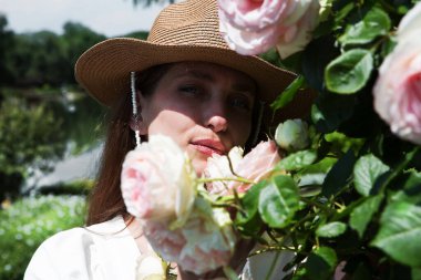 Genç ve seksi bir kadının portresi Bahçede çiçek açan güllerin kokusunun tadını çıkarıyor.