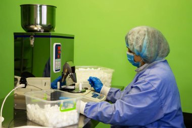 Araştırma asistanı kavanozları ilaçlarla doldurur. Otomatik ilaç teçhizatı üzerine ilaçlar. Tıbbi hazırlıkların üretimi ve üretimi.