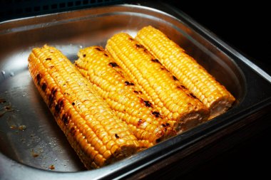 Izgarada pişirilmiş mısır koçanının üzerinde iştah açıcı mısır. Fast food. Gidecek sokak yemeği. Izgarada pişmiş sıcak hazır yemek..