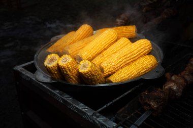 Siyah arka planda izole edilmiş dumanla bir kazanda kaynatılmış mısır kafalar. Fast food. Gidecek sokak yemeği. Izgarada pişmiş sıcak hazır yemek..
