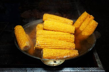 Siyah arka planda izole edilmiş dumanla bir kazanda kaynatılmış mısır kafalar. Fast food. Gidecek sokak yemeği. Izgarada pişmiş sıcak hazır yemek..