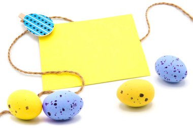 Beyaz bir arka planda saçılmış renkli yumurtalarla çamaşır mandallarına ip asılmış boş bir kart. Uzayı kopyala Metin için boş alan. Mutlu Paskalyalar! Paskalya geleneksel el yapımı boyanmış yumurtalar.