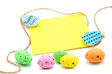 Beyaz arka planda izole edilmiş çeşitli renkli yumurtalarla birlikte çamaşır mandallarında iple dolu boş bir kart. Uzayı kopyala Metin için boş alan. Mutlu Paskalyalar! Paskalya geleneksel el yapımı boyanmış yumurtalar.