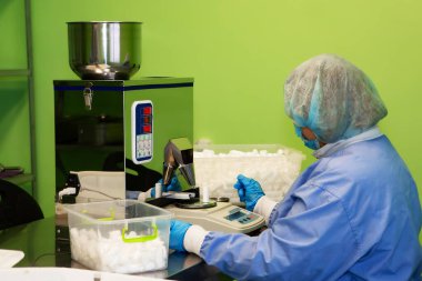 Araştırma asistanı kavanozları ilaçlarla doldurur. Otomatik ilaç teçhizatı üzerine ilaçlar. Tıbbi hazırlıkların üretimi ve üretimi.