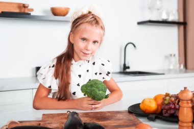 Küçük güzel kız mutfakta yemek pişirirken brokoli tutuyor. Sağlıklı beslenme. Vitamin yiyecekler sağlığınız için iyidir..