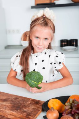 Küçük güzel kız mutfakta yemek pişirirken brokoli tutuyor. Sağlıklı beslenme. Vitamin gıdaları sağlığınız için iyidir. Zindelik.