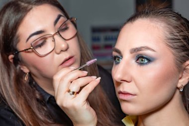Makyaj sanatçısı, profesyonel bir kuaförde genç ve güzel bir kıza makyaj yapıyor. Güzellik, moda ve cilt bakımı endüstrisi. Makyaj sanatçısının işi..