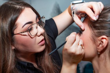 Makyöz, profesyonel bir kuaförde güzel bir kıza kirpik uzatıyor. Güzellik, moda ve cilt bakımı endüstrisi. Makyaj sanatçısının işi. Takma kirpikler..