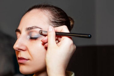 Makyaj sanatçısı, profesyonel bir kuaförde genç ve güzel bir kıza makyaj yapıyor. Güzellik, moda ve cilt bakımı endüstrisi. Makyaj sanatçısının işi. Göz kapaklarına gözkapağı uygulanıyor.