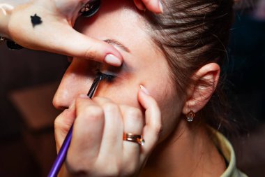 Makyaj sanatçısı, profesyonel bir kuaförde genç ve güzel bir kıza makyaj yapıyor. Güzellik, moda ve cilt bakımı endüstrisi. Makyaj sanatçısının işi. Göz kapaklarına gözkapağı uygulanıyor.