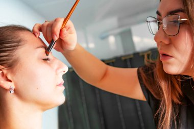 Makyaj sanatçısı, profesyonel bir kuaförde genç ve güzel bir kıza makyaj yapıyor. Güzellik, moda ve cilt bakımı endüstrisi. Makyaj sanatçısının işi. Göz kapaklarına gözkapağı uygulanıyor.
