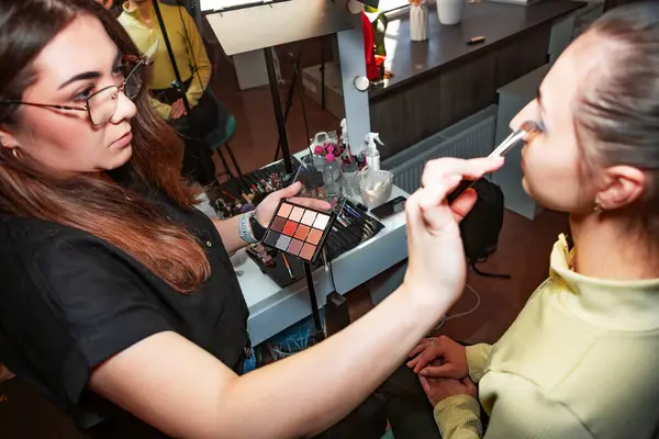 Makyaj sanatçısı, profesyonel bir kuaförde genç ve güzel bir kıza makyaj yapıyor. Güzellik, moda ve cilt bakımı endüstrisi. Makyaj sanatçısının işi. Göz kapaklarına gözkapağı uygulanıyor.