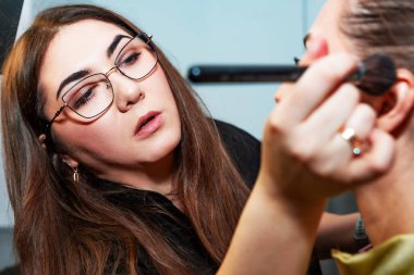 Makyaj sanatçısı, profesyonel bir kuaförde genç ve güzel bir kıza makyaj yapıyor. Güzellik, moda ve cilt bakımı endüstrisi. Makyaj sanatçısının işi. Yanaklara allık sürüyorum..