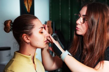 Makyaj sanatçısı, profesyonel bir kuaförde genç ve güzel bir kıza makyaj yapıyor. Güzellik, moda ve cilt bakımı endüstrisi. Makyaj sanatçısının işi. Göz kapaklarına gözkapağı uygulanıyor.