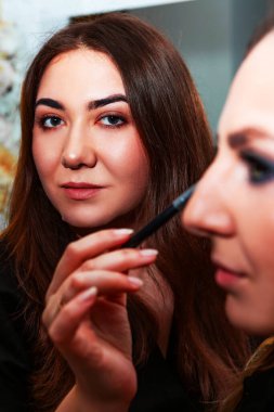 Makyaj sanatçısı, profesyonel bir kuaförde genç ve güzel bir kıza makyaj yapıyor. Güzellik, moda ve cilt bakımı endüstrisi. Makyaj sanatçısının işi. Göz kapaklarına gözkapağı uygulanıyor.