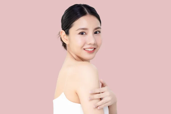 美丽的年轻亚洲女人在粉红背景的肩部涂上乳液 — 图库照片