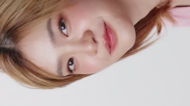 Yavaş çekim beyaz arka planda genç Asyalı kızın yüzüne yakın çekim. Dikey görüntüler.