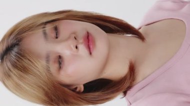 Yavaş çekim beyaz arka planda genç Asyalı kızın yüzüne yakın çekim. Dikey görüntüler.