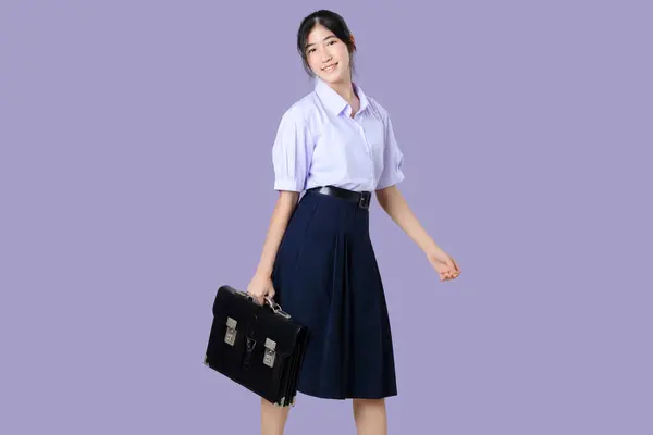 紫色の背景に隔離された学校のユニフォームの幸せな若いアジアの学生の女の子の肖像画 ストック写真