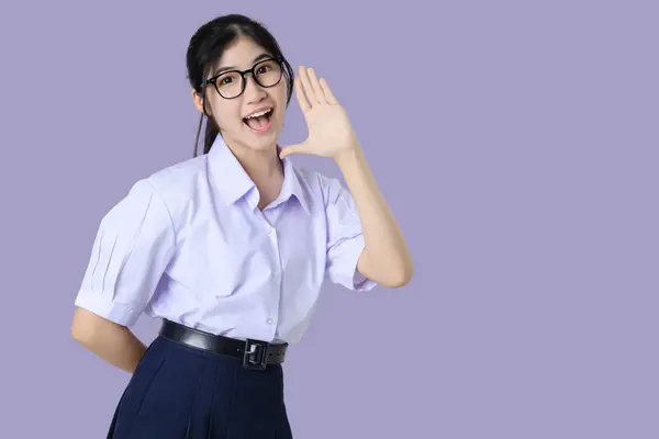ハッピーな若いアジアの学生の女の子の肖像画 学校の制服で手を上げる 紫色の背景に隔離された叫び声 ストック画像