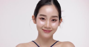 Işıl ışıl cildi ve K-Güzeli olan güzel Asyalı kızın yavaş çekimleri. Ticari güzellik reklamları için izole edilmiş beyaz arka planda makyaj stili..