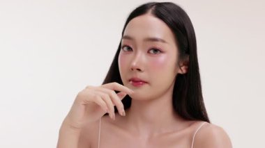 Genç Asyalı bir kadının yumuşak ve minimal stüdyo ortamında doğal kozmetik krem sürdüğü bir cilt bakımı videosu. Güzelliği, kendine bakımı ve organik cilt ürünlerini teşvik etmek için idealdir..