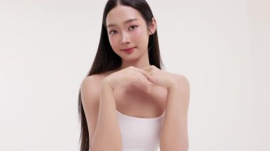Genç Asyalı bir kadının yumuşak ve minimal stüdyo ortamında doğal kozmetik krem sürdüğü bir cilt bakımı videosu. Güzelliği, kendine bakımı ve organik cilt ürünlerini teşvik etmek için idealdir..