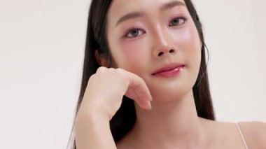 Genç Asyalı bir kadının yumuşak ve minimal stüdyo ortamında doğal kozmetik krem sürdüğü bir cilt bakımı videosu. Güzelliği, kendine bakımı ve organik cilt ürünlerini teşvik etmek için idealdir..