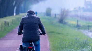 Hollanda, Gelderland 'daki Polder arazisinde bisiklet yolunda bisiklet süren kimliği belirsiz bir adam var.