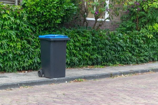 empty bin container standing next on the sidewalk next to the road in the netherlands