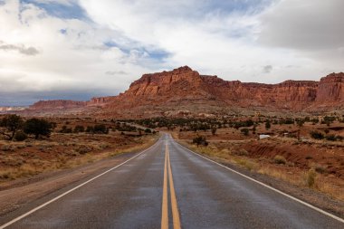 Utah, Zion Ulusal Parkı 'nın çarpıcı kırmızı kaya oluşumlarına uzanan pitoresk bir yol. Her iki tarafında geniş bir gökyüzü ve engebeli bir arazi var..