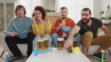 Dört arkadaş TV 'de spor izliyor, bira ve atıştırmalıkların tadını çıkarıyor, bazıları telefonda, diğerleri coşkuyla el kol hareketi yapıyor. Atmosfer dinamik ve çekici, canlı bir deneyim yaratıyor.