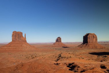 Arizona 'daki Navajo Anıt Parkı açık mavi gökyüzü altındaki ikonik kırmızı kaya oluşumlarının nefes kesici bir panoramik görüntüsünü sunuyor. Açık hava maceraları ve turistik yerler için mükemmel.