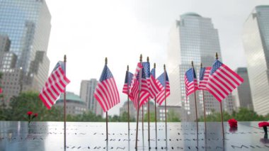 NEW YORK, ABD - 11 Eylül 2023 Amerikan bayrakları, yumuşak odaklı arka planda yükselen yansıtıcı gökdelenler ile düşen kahramanların anısına dalgalanıyor. Yavaş Hareket, 4K HAM. 