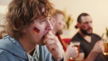 Yüzleri Alman bayrağıyla boyanmış bir grup hevesli arkadaş, takımlarına tezahürat yaparken heyecan ve yoldaşlık sergileyerek bir futbol maçını izlemek için evlerinde toplanıyor.