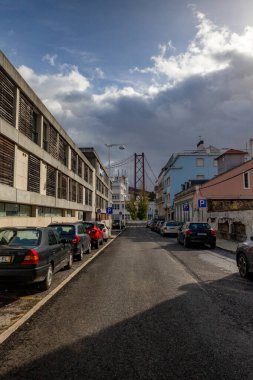 Büyüleyici görüntü, geleneksel ve modern mimari, arabalar ve hareketli başkentte parçalı bulutlu bir gökyüzünün altında bir köprü karışımı ile pitoresk bir Lisbon caddesini gösteriyor.